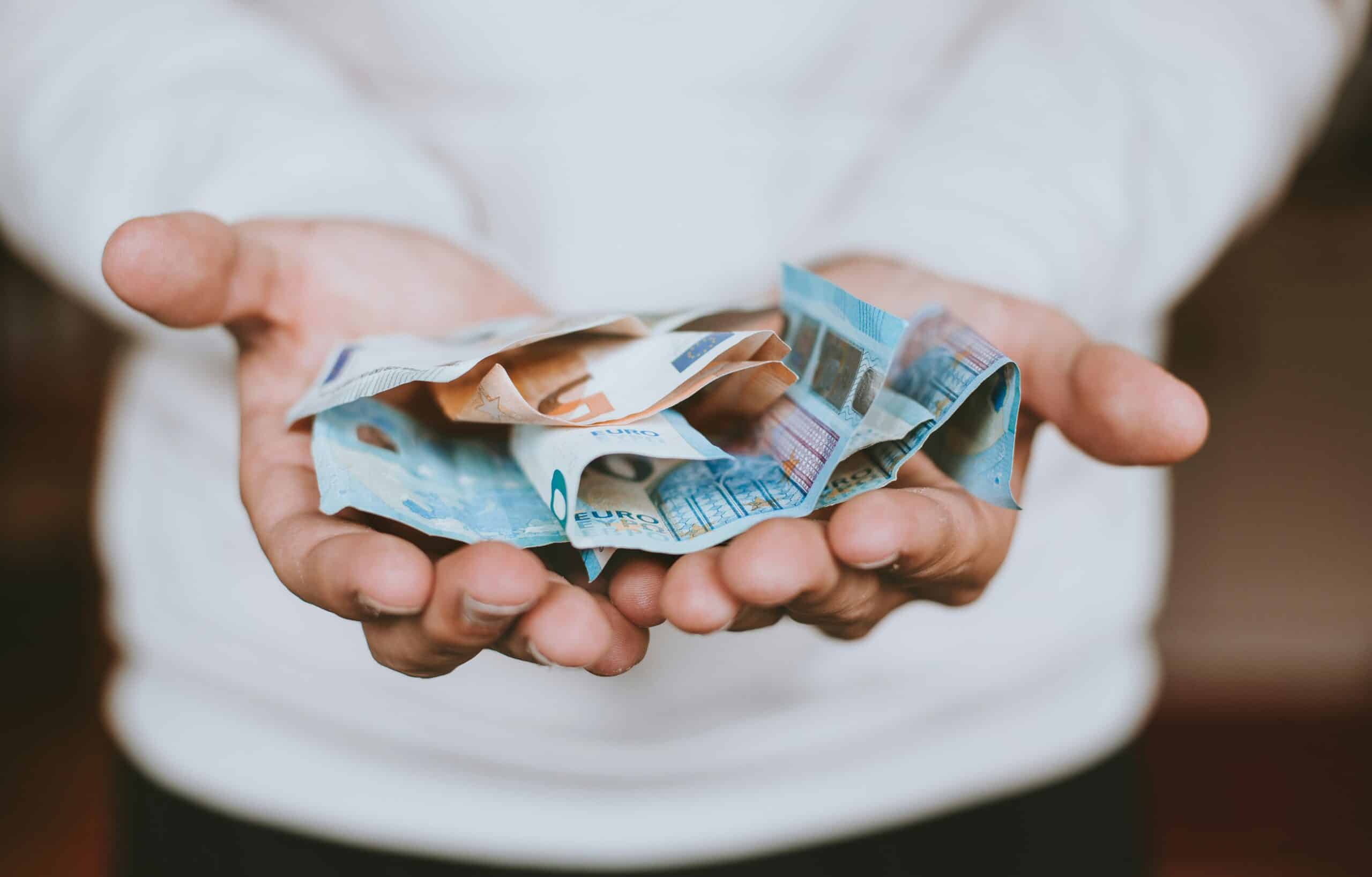 A person wearing a white shirt holds several crumpled euro banknotes in their open hands, highlighting the importance of financial education and smart money management.