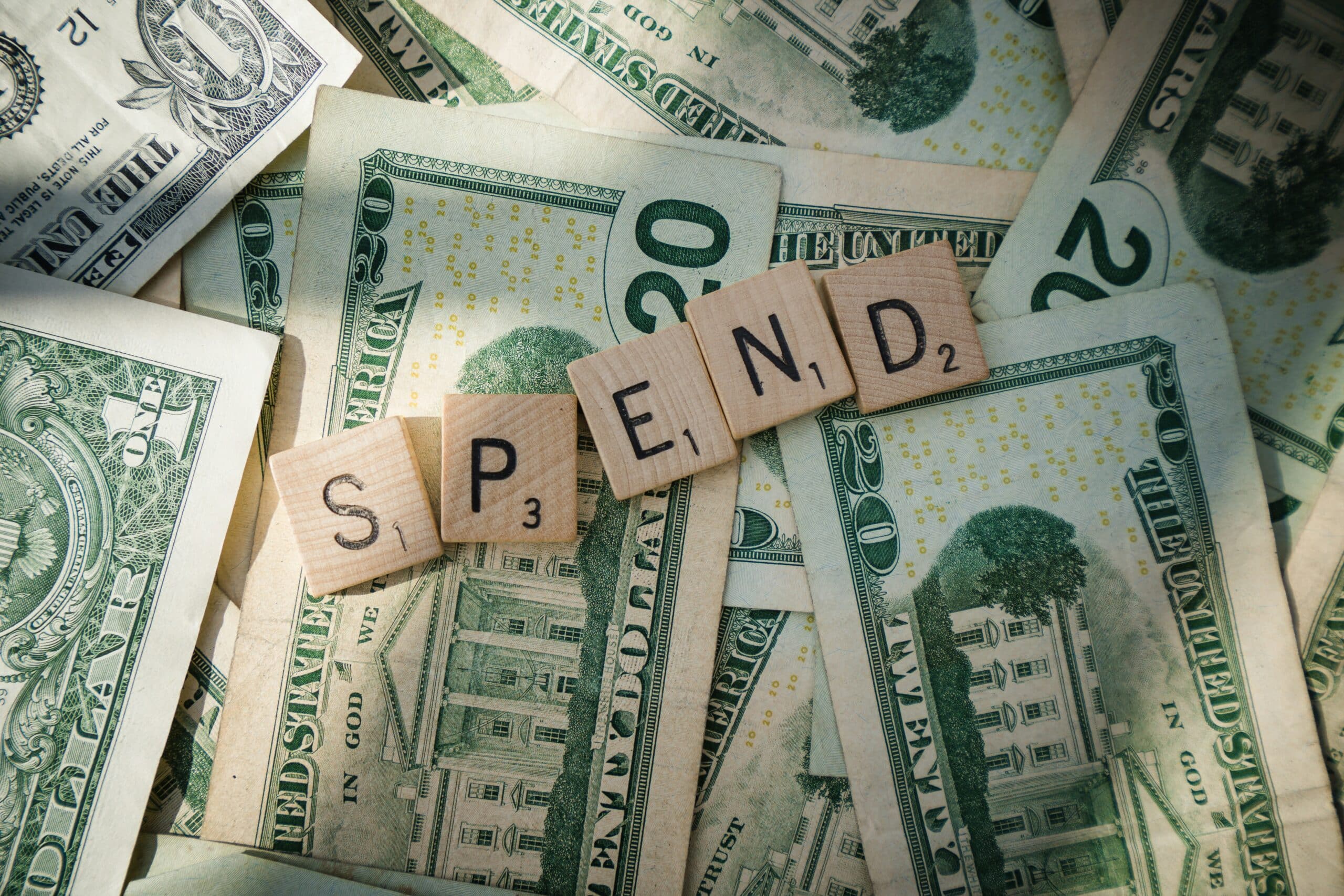 Scrabble tiles spelling SPEND are arranged on U.S. dollar bills, visually representing concepts like money, financial education, and smart spending habits.